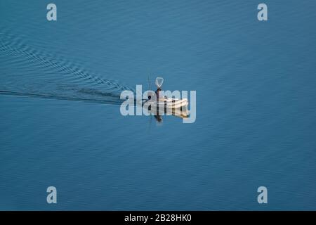 Pêcheur au milieu d'un lac bleu pêchant sur un bateau à moteur gonflable en caoutchouc. Banque D'Images