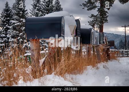 Une longue rangée de boîtes aux lettres rurales sur des postes bruts dans la neige sous les lignes électriques par la clôture de rail fendu Banque D'Images