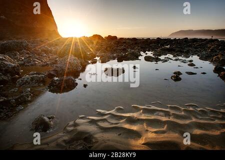 Le soleil se couche sur l'océan Pacifique près de Haystack Rock, près de Cannon Beach, sur la côte de l'Oregon, avec la marée bien éloignée et les rochers couverts par le barapogée expos Banque D'Images