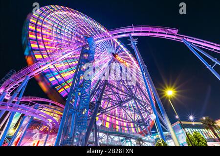 Vue de dessous du géant coloré Ferris Wheel and Roller Coaster illuminé la nuit dans le district de Minato Mirai. Banque D'Images