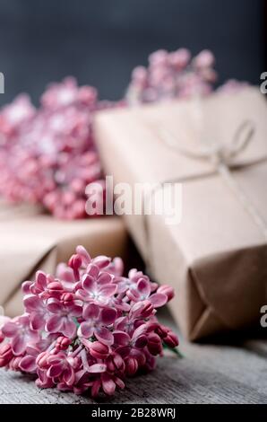 Boîtes cadeaux faites à la main, revêtues de papier brun artisanal, décorées de fleurs de lilas pourpre fraîches sur une surface en bois vintage. Vacances de printemps arrière-plan. Banque D'Images