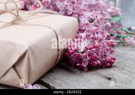 Boîtes cadeaux faites à la main, revêtues de papier brun artisanal, décorées de fleurs de lilas pourpre fraîches sur une surface en bois vintage. Vacances de printemps arrière-plan. Banque D'Images