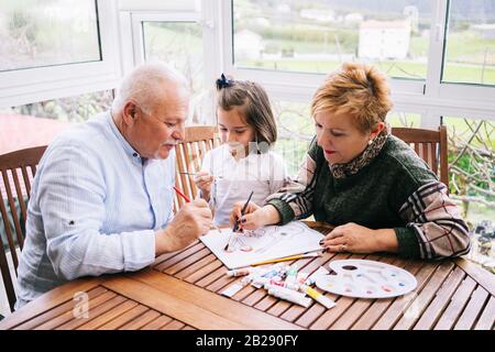 Une petite fille avec ses grands-parents peindre quelques dessins sur la terrasse de sa maison avec de la peinture aquarelle Banque D'Images