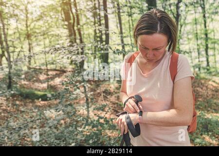 Randonneur féminin en vérifiant un tracker de fitness intelligent tout en faisant du trekking dans la forêt Banque D'Images