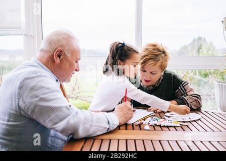 Une petite fille avec ses grands-parents peindre quelques dessins sur la terrasse de sa maison avec de la peinture aquarelle Banque D'Images