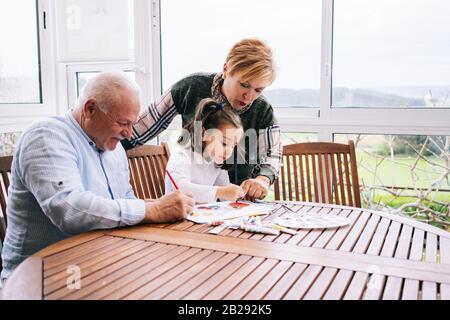 Une petite fille avec ses grands-parents peindre quelques dessins sur la terrasse de sa maison avec de la peinture aquarelle Banque D'Images