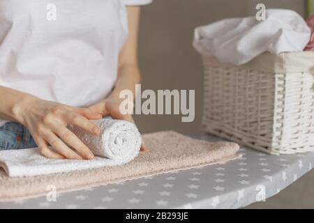 Femme roulante de serviettes propres debout à la planche à repasser. Service de blanchisserie ou nettoyage des articles ménagers concept Banque D'Images