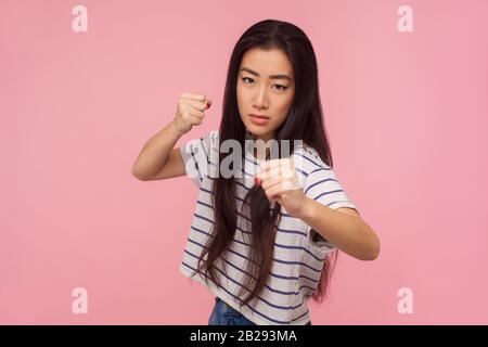 Je vais vous poinçonner ! Portrait d'une fille en colère avec de longs cheveux dans un t-shirt rayé debout avec un geste de boxe, des poings tentants prêts à se battre, menaçant à Banque D'Images