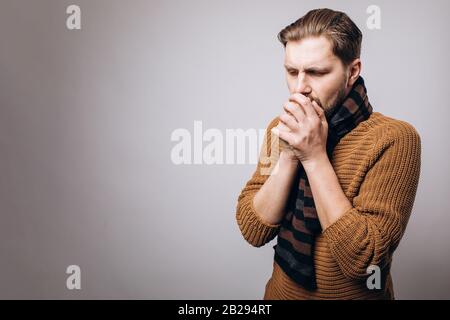 Portrait d'homme barbu mûr dans un pull chaud tricoté et une écharpe toussant au studio avec fond gris. Concept de maladie et de soins de santé Banque D'Images
