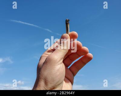 Main humaine tenir la cigarette de tabac sur fond de ciel bleu, fumer accro Banque D'Images