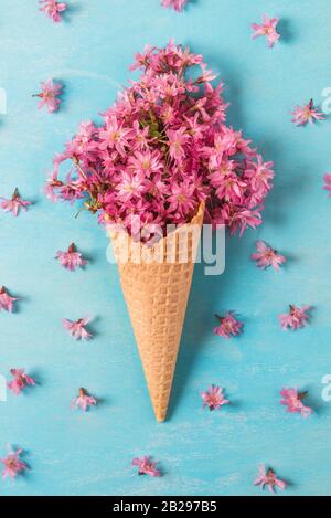 Cornet de crème glacée avec des fleurs de printemps fleurs de cerisier sakura ou rose sur fond bleu. Concept de printemps minimes. Télévision lay. Vue de dessus l'orientation verticale. Banque D'Images