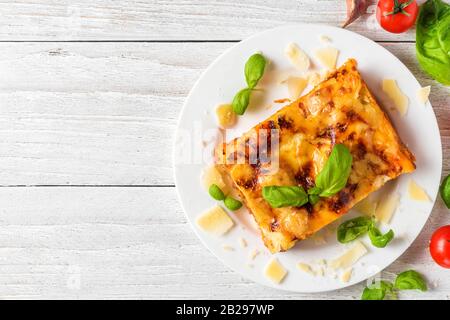 Lasagnes à la viande maison au basilic frais et au parmesan dans une assiette sur table en bois blanc. Vue sur le dessus. Cuisine italienne. Banque D'Images