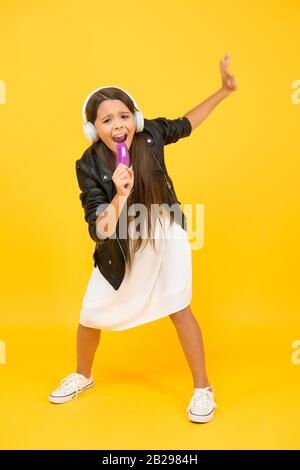 Chant karaoké en ligne. Musique dans les écouteurs sans fil. Peigne pour enfant comme microphone. Musique pour enfant dans le casque. Petite fille, musique DJ. Concept de bonne enfance. Retour à l'école. Accessoire musical. Banque D'Images