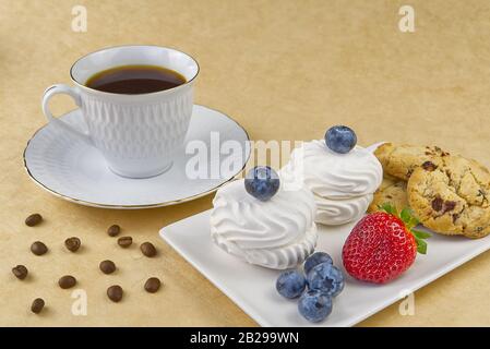 tasse à café blanche avec petit déjeuner à bordure dorée, café et biscuits bize avec framboises et bleuets Banque D'Images