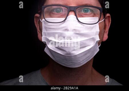 Homme caucasien avec yeux bleus et lunettes regardant directement dans l'appareil photo avec masque médical sur. Embout buccal de filtre couvrant la bouche et le nez Banque D'Images