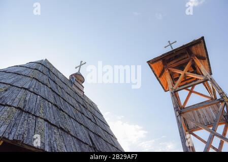 Image plus large d'un toit de cabane en bois construit à partir de foin avec une croix sur le dessus comme église médiévale en Serbie avec clocher debout à côté du bâtiment Banque D'Images