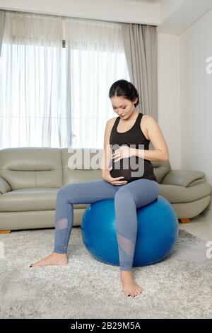 Jeune femme vietnamienne enceinte faisant un exercice de détente sur le ballon de fitness à la maison Banque D'Images