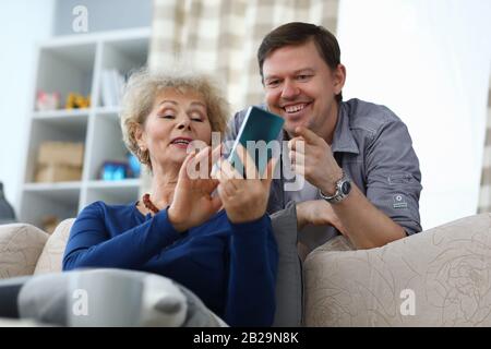 La mère âgée montre une photo au téléphone au fils adulte Banque D'Images