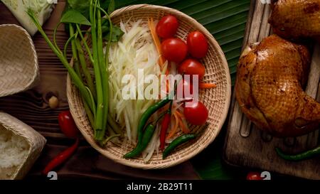 Vue de dessus des ingrédients salade Somtum ou papaye, cuisine traditionnelle thaïlandaise avec poulet grillé sur plateau en bois Banque D'Images