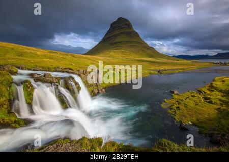 Kirkjufell montage contre gris nuages arrière-plan. Cascades photographiées avec une longue exposition en premier plan. Banque D'Images