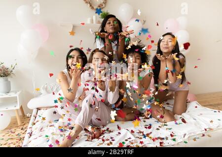 Portrait heureux diverses filles soufflant des confettis à l'appareil photo à la fête Banque D'Images