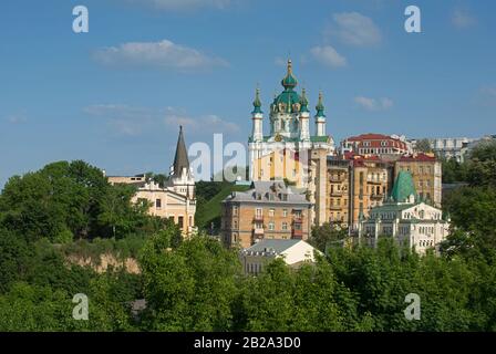 Vue générale de la descente d'Andriyivskyy avec l'Église Saint-André. Premier plan - feuillage de printemps. Arrière-plan - ciel bleu. Banque D'Images