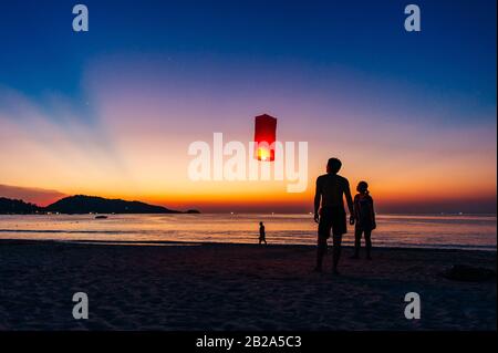 Silhouettes de personnes sur la plage. Lancement de ballons d'air chaud en papier de riz dans le ciel au coucher du soleil sur une plage en Thaïlande Banque D'Images