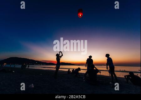 Silhouettes de personnes sur la plage. Lancement de ballons d'air chaud en papier de riz dans le ciel au coucher du soleil sur une plage en Thaïlande Banque D'Images