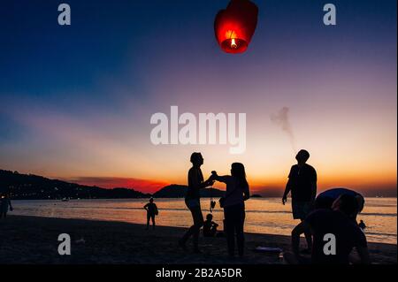 Silhouettes de personnes sur la plage. Lancement de ballons d'air chaud en papier de riz dans le ciel au coucher du soleil sur une plage en Thaïlande Banque D'Images