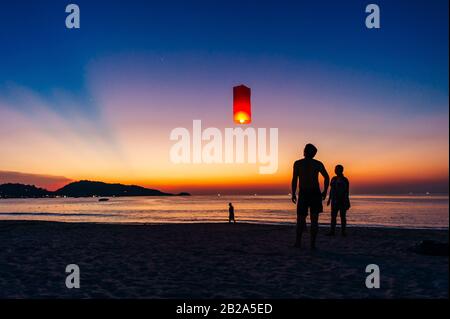 Silhouettes de personnes sur la plage. Lancement de ballons d'air chaud en papier de riz dans le ciel au coucher du soleil sur une plage en Thaïlande Banque D'Images