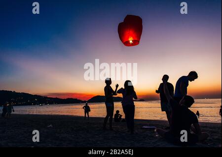 Silhouettes de personnes sur la plage. Lancement de ballons d'air chaud en papier de riz dans le ciel au coucher du soleil sur une plage en Thaïlande Banque D'Images