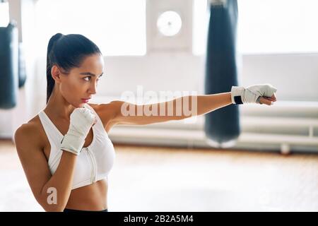 Boxeur féminin pratiquant ses poinçons dans un studio de boxe. Femme athlétique qui fait un coup direct. Concept sportif Banque D'Images