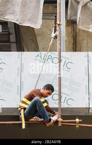 Un ouvrier est suspendu d'un mât d'échafaudage avec un harnais de sécurité, une corde et un crochet au-dessus d'un chantier, Bangkok, Thaïlande. Banque D'Images