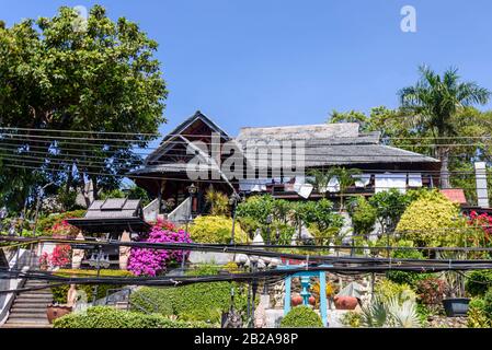 Câbles électriques désordonnés et mal rangés accrochés à un poteau électrique à l'extérieur d'une jolie maison et jardin sur une colline, Kata, Phuket, Thaïlande Banque D'Images