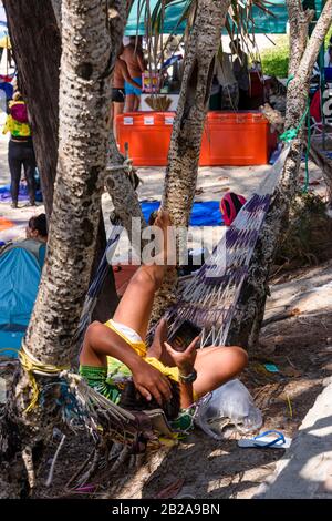 Un homme regarde son smartphone alors qu'il se détend sur un hamac pendant une pause au bar d'un café de plage, Thaïlande Banque D'Images