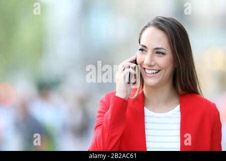 Portrait d'une heureuse femme portant une veste rouge parlant sur le téléphone en regardant le côté dans la rue Banque D'Images