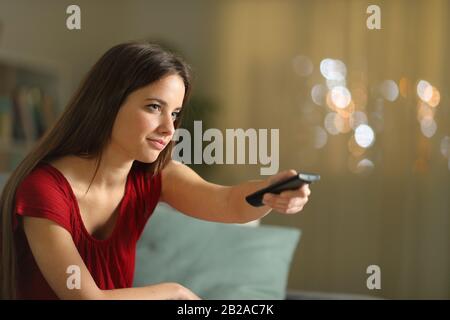 Femme changeant de chaîne de télévision avec télécommande assis sur un canapé à la maison dans la nuit Banque D'Images