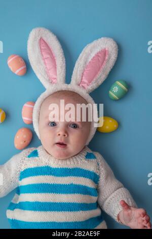 Joli bébé portant des oreilles de lapin de pâques entourées d'œufs de pâques. Banque D'Images