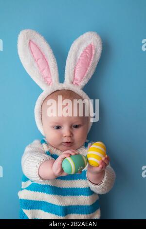 Joli bébé portant des oreilles de lapin de pâques entourées d'œufs de pâques. Banque D'Images