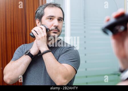 40 ans d'homme se raser le matin à l'aide d'un rasoir électrique Banque D'Images