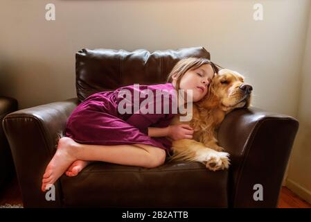 Une fille s'est rebouclés dans un fauteuil avec un chien doré Banque D'Images