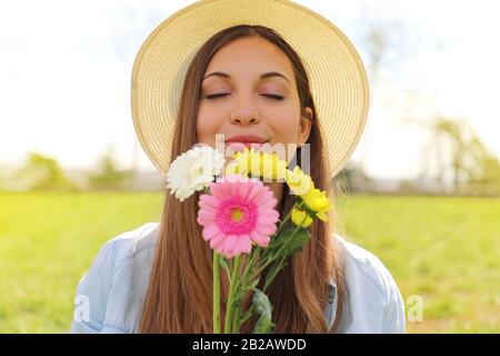 Belle jeune fille avec des yeux fermés et chapeau odeur bouquet de fleurs au printemps Banque D'Images