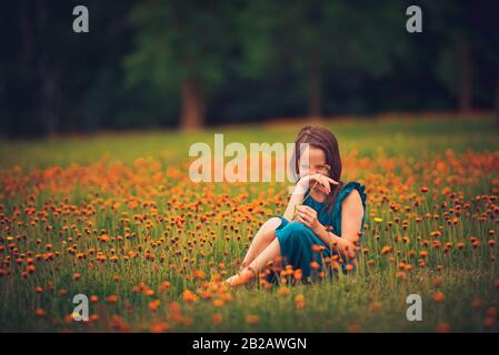 Heureuse fille assise dans un pré avec des fleurs sauvages riant, États-Unis Banque D'Images