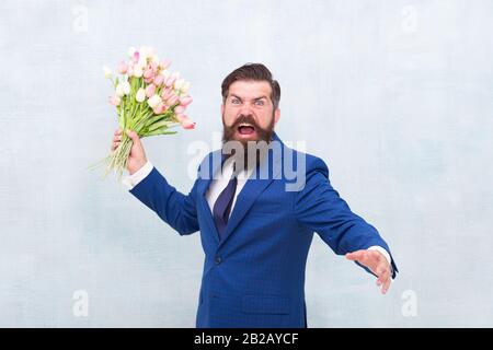 Des vacances de haine. Journée pour femme. 8 Mars. Homme barbu en colère avec des fleurs. Fêtez le printemps. Échec de la date. Irritée, l'homme barbu agacé avec bouquet de tulipes. Concept déçu. Date d'échec. Banque D'Images