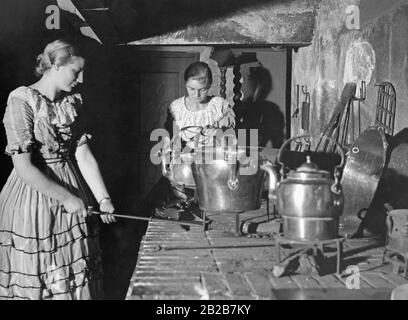 Deux femmes cuisinent dans la cuisine de la maison Uphagen du XIXe siècle. La Maison Uphagen a été construite dans les années 1870 et 1880 dans la Langgasse de Gdansk, puis transformée en musée. Dans la cuisine il y a un ensemble d'ustensiles de cuisine, qui a été utilisé pour cuisiner de grandes portions de nourriture. Banque D'Images