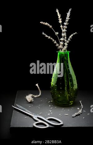 Lavande séchée dans une bouteille verte avec ciseaux et corde photographiée en studio avec lumière sombre moody. Banque D'Images