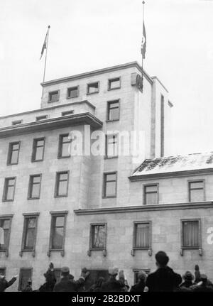 Les drapeaux de victoire sont hoirés sur le toit de la Chancellerie du Nouveau Reich comme signe de la victoire en Sarre. Sur la droite se trouve le drapeau de la swastika, sur la gauche se trouve le Reichsdienstflagge (drapeau du service Reich) du Reich allemand. Les partisans rendent le salut nazi tout en écoutant. Banque D'Images