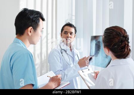 Pulmonologue sérieux et inquiet montrant la radiographie thoracique et demandant aux collègues de l'aider à comprendre le diagnostic Banque D'Images
