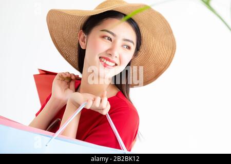 Portrait de la jeune femme asiatique belle portant une robe longue rouge tenant des sacs de shopping isolés sur fond blanc. Les femmes font du shopping en été Banque D'Images