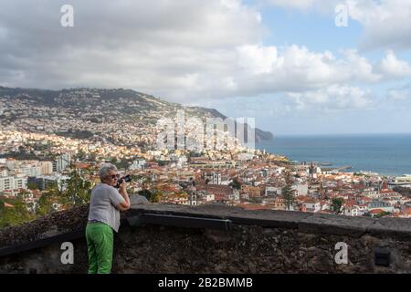 Les femmes se tenant sur un point de vue avec une caméra, en regardant la vue sur funchal Madeira, Portugal et la mer avec un ciel nuageux en arrière-plan. Banque D'Images